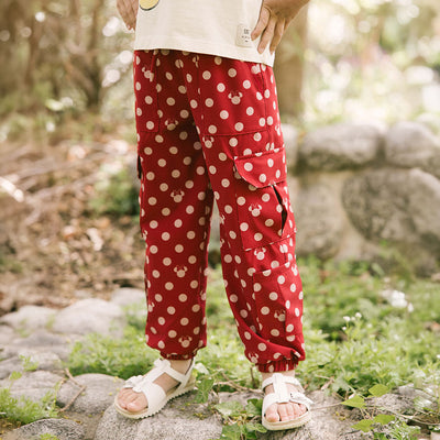 Child wearing cute kids pants for Disneyland in red polka dot print with hidden Minnie Mouse icons throughout on a blurred garden background
