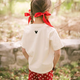 Close up back view of young girl wearing a white Disney t-shirt with embroidered Mickey ears on the back on a blurred natural background
