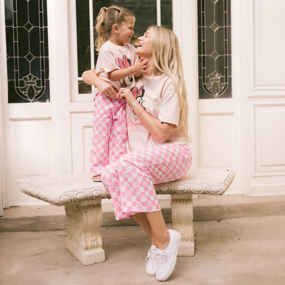 Mom and daughter sitting on a bench wearing matching Minnie Mouse outfits for families in pink 