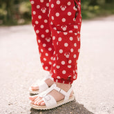 Close up of child standing on the street wearing white sandals and red polka dot Minnie Mouse pants with lots of pockets