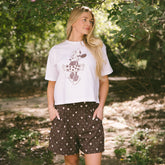 Woman standing in a forest wearing a cute Minnie Mouse t shirt and brown, subtle Disney shorts with Minnie Mouse print.