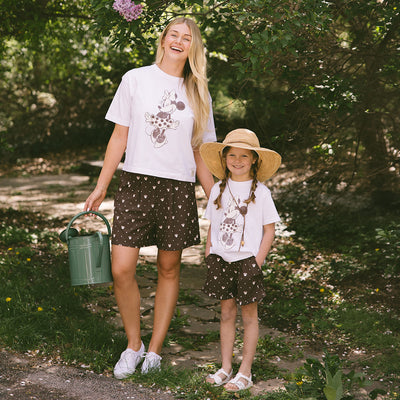 Woman and child standing outdoors wearing matching Disneyland outfits—kids Minnie Mouse t-shirt and matching neutral kids Disney shorts with Minnie Mouse print.