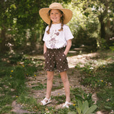 Young girl standing on a path in a garden wearing a wide-brimmed hat and wearing a cute kids Disney outfit. 