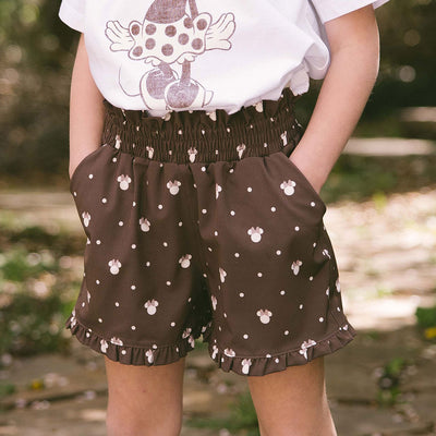 Child wearing brown kid's Disney shorts with subtle Minnie Mouse print on a blurred green background. 