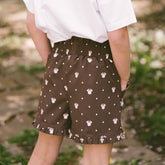 Close up back view of child wearing subtle kids Disney outfit—brown kids Minnie shorts on a blurred greenery background