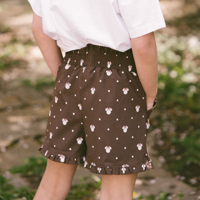 Close up back view of child wearing subtle kids Disney outfit—brown kids Minnie shorts on a blurred greenery background