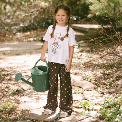 Child wearing a cute kid's Disney outfit—kid's Disney pants in Minnie Mouse print holding a watering can in a garden.