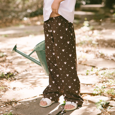 Child standing in a garden wearing kid's Disney pants—brown wrinke-free kids pants in Minnie Mosue print are perfect for Disneyland. 
