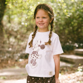 Child wearing a kid's Minnie Mouse t-shirt on a blurred greenery background.