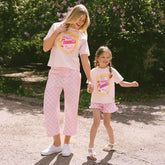 Mom and daughter wearing matching Disneyland outfits—pink Cinderella shirt for kids and pink check bottoms standing in a garden.
