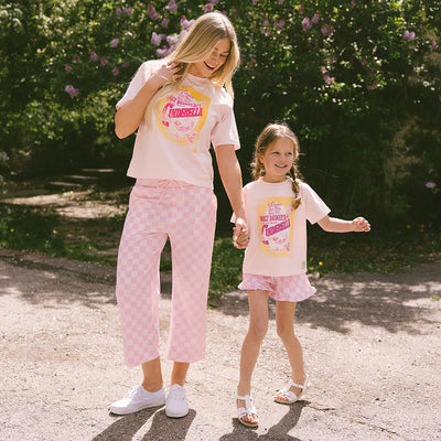 Mom and daughter wearing matching Disneyland outfits—pink Cinderella shirt for kids and pink check bottoms standing in a garden.