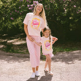 Woman and child wearing matching pink Cinderella t-shirts for Disneyland and pink check bottoms in a garden setting.