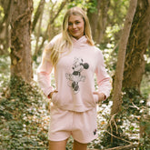 Woman wearing pink Disney sweatshirt with screen printed Minnie Mouse and matching womens Disney shorts with Minnie Mouse icon, standing in a forest.