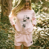 Woman wearing a light pink Minnie Mouse hoodie and shorts in a forest setting