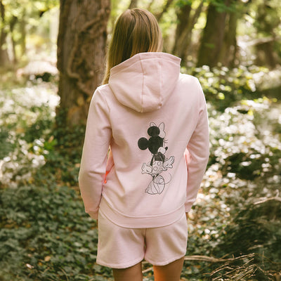 Back view of woman standing in a forest wearing a pink Minnie sweatshirt and matching pink shorts. 