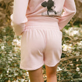 Back view of women's light pink shorts that are the perfect subtle Disneyland outfit on a blurred garden background
