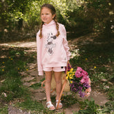 Young girl in a kid's pink Disney with a Minnie Mouse design, standing outdoors holding flowers.