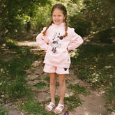 Child standing on a forest path wearing a kid's Minnie Mouse sweatshirt in pink with matching kid's Disney shorts. 