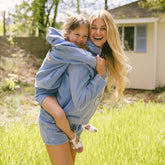Woman holding a child on her back while wearing matching Disney outfits—kid's Mickey Mouse sweatshirt and matching shorts. 