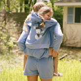Mom carrying a child on her back, they are wearing matching Disney outfits—blue Mickey Mouse hoodies and blue Mickey Mouse shorts. 