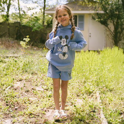 Child standing in a green field wearing a kids Disneyland outfit—kid's Mickey Mouse hoodie with matching kid's Mickey Mouse shorts. 