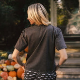 Back view of Perfect Jester Tee in vintage black showcasing short sleeves on a model with a pumpkin display background