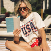 Woman reading a book outdoors wearing a 'USA 1776' t-shirt and red stars swimsuit