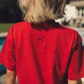 Person wearing a red shirt with a star emblem, standing by a poolside.