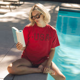 Woman in a red 'USA' t-shirt reading by a pool