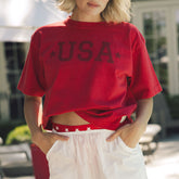 Woman wearing a red women's USA t-shirt with a blurred outdoor background