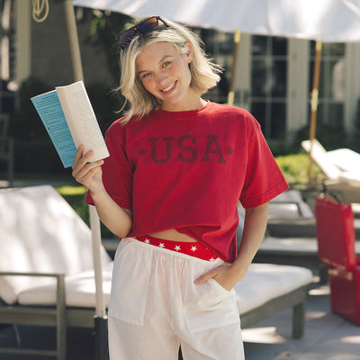 Woman in a red USA women's t-shirt holding a book outdoors.