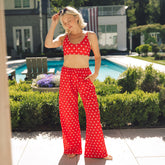 Woman standing by a pool wearing cute 4th of july outfit—red flowy pants with a star pattern and matching swimsuit. 