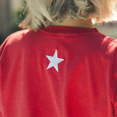 Red shirt with a white star on the back, worn by a woman on a blurred background.