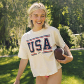 Woman wearing a 'USA 1776' t-shirt holding a football outdoors.