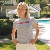 Woman wearing a striped t-shirt with 'america' printed on it, standing outdoors near a pool.