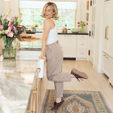 Woman in a kitchen wearing a white top and brown linen balloon pants, with flowers and a vase on the counter.
