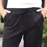 Black knit lounge pants with an elastic drawstring waistband, shown on a model with hands in pockets.