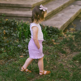 Young child in a kid's Minnie tank top and purple gingham kid's shorts walking in a garden