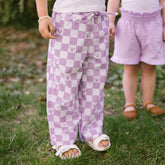 Two children wearing purple checkered pants with Minnie Mouse print standing on grass.