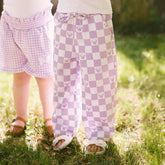 Two young girls wearing coordinating Disney outfits—kids Disney shorts and kids Disney pants in purple gingham with Minnie Mouse details.