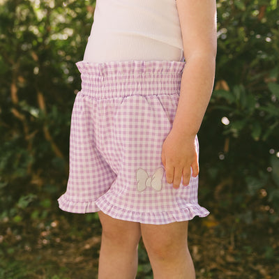 Close up of child in a garden wearing purple gingham Minnie Mouse shorts for kids.