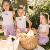 Three young girls in matching Disney outfits with animals in a basket outdoors.