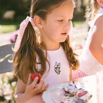 Close up of a young girl wearing a kids Daisy Duck shirt with pink bows in her hair on a blurred natural background