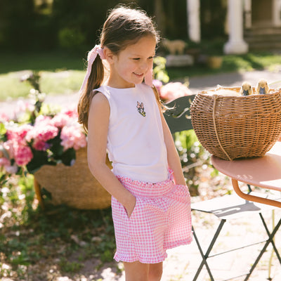 Young girl in a garden setting wearing a kids Disney top with Daisy Duck embroidery and pink gingham kid's Disney shorts next to a basket with baby ducks.