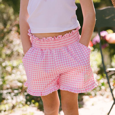 Child wearing the perfect Disneyland shorts for kids in pink gingham with a Minnie Mouse bow on a blurred garden background