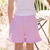 Close up back view of child wearing pink gingham kid's shorts on a blurred garden background