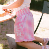 Child kneeling on a patio chair wearing pink gingham Minnie Mouse shorts for kids.