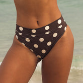 Brown bikini bottom with white polka dots worn by a person on a beach.