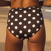 Person wearing a brown swimsuit with white polka dots on a beach.