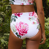 Floral bikini set with pink flowers on a white background, worn by a person against a green leafy background.